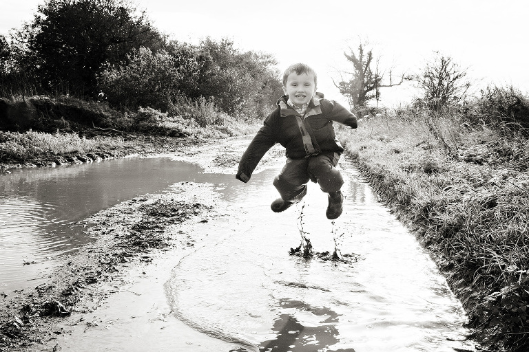 A very happy boy jumping in a puddle